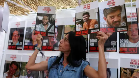 Reuters Einav Zangauker, the mother of hostage Matan Zangauker, holds up posters as she stands inside sukkah at a rally outside Israeli Prime Minister Benjamin Netanyahu's residence in Jerusalem (5 October 2025)