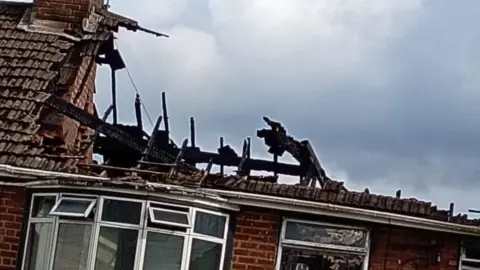 A severely damaged roof of a house with burnt beams, charred from a fire