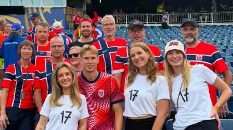 Supplied A group of people wearing Norwegian flag colours are posing for a photo in a stadium at the World Cup.
