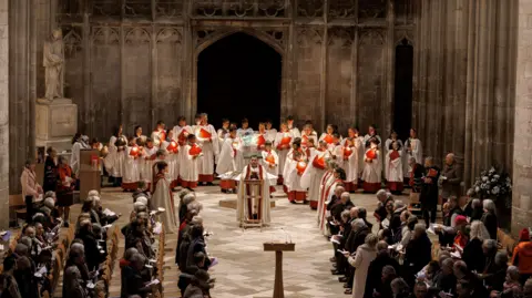 Clive Barzillia, Gloucester Cathedral Parishioners and choir members are seen standing and singing inside Gloucester Cathedral as part of the Candlemas service. The image is taken from a slightly raised position