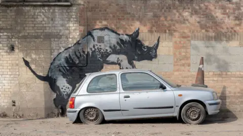 Banksy artwork of rhino mounting car