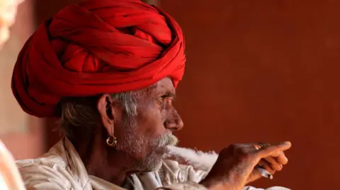 Getty Images A man in a red turban smokes a cigarette
