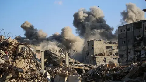 AFP, izmantojot Getty Images, Gazas joslas centrālajā daļā virs šķembu kaudzēm un pussabrukušām ēkām kūsā dūmi.