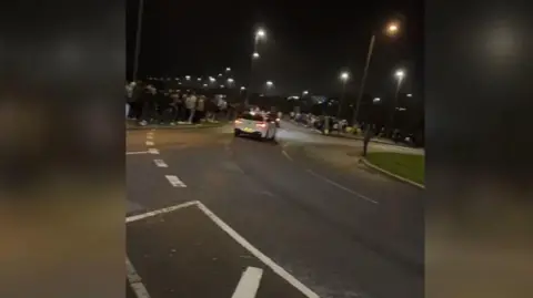 Avon and Somerset Police A still from a video of a white car spinning out of control towards a crowd of people