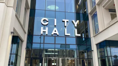 The entrance of Sunderland City Council headquarters. The sign above the glass fronted building reads "city hall".

