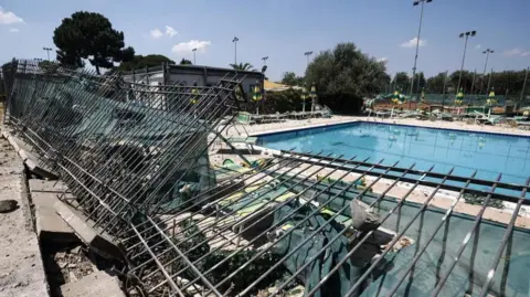 EPA / Shutterstock Picture shows damage to a nearby sports centre after the explosion. The roof is completely shattered and there is debris scattered around a swimming pool