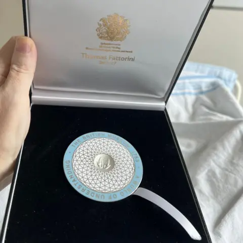 Ittai Gradel The medal awarded to Dr Ittai Gradel in a presentation box - it is circular, pale blue on the outside with the centre in white and gold, similar in design to the roof of the extension to the British Museum - curved lattice work