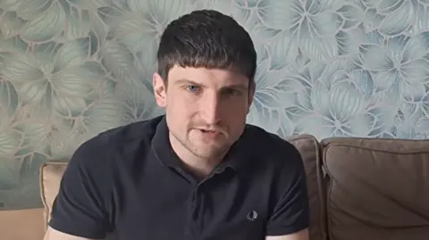 OTHER A young man looks at the camera. He has relatively short, dark hair and is wearing a dark polo shirt.