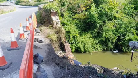 Canal & River Trust Orange traffic cones and barrier next to a road and crumbling bridge, with the canal water at the bottom