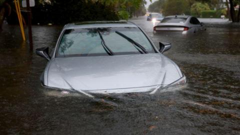A car is left half submerged after flash flooding following record rainfall in Florida