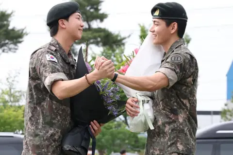 RM, left, dressed in military uniform, shakes hands with V, right, also in military uniform