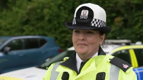 A female police constable looking to the side of the camera. There are blurred out cars in the background.