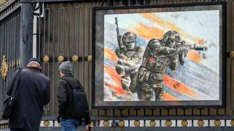 EPA-EFE/REX/Shutterstock People walk past an electronic screen showing a graphic drawing of Russian soldiers in downtown Moscow