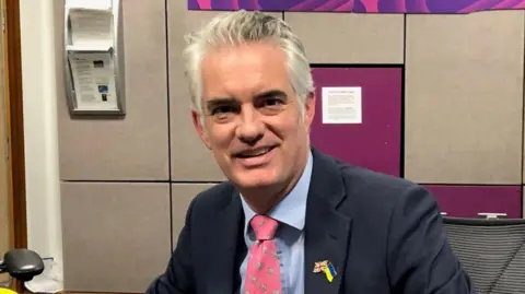 MP James Cartlidge wearing a navy suit during a visit to the BBC Radio Suffolk studio in Ipswich.