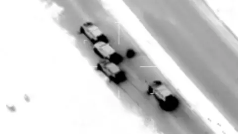 A black and white image from a CCTV video from above showing four cars on a dual carriage motorway