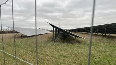 North Angle Solar Farm panels in a field, behind a wired fence.