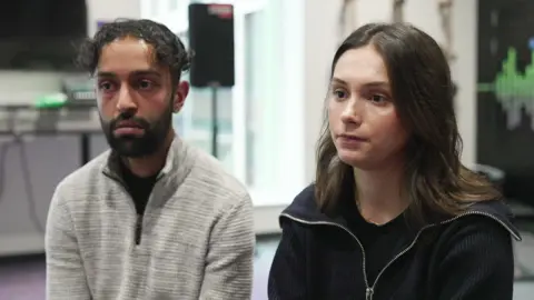 Bipin Khanal, in a grey top and with dark hair and beard, sits beside Leonita Metaj, who has long dark hair, in a youth centre. 