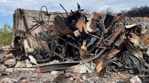 Piles of twisted blackened metal at the Salthouse Mills site in Barrow, which has been hit by a fire. There is debris all around the site, including piles of red bricks.