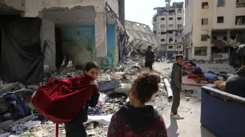 AFP is a Palestinian girl carrying a bag while children walk through the buildings that were damaged and destroyed by West Gabalia, in northern Gaza (February 26, 2025)