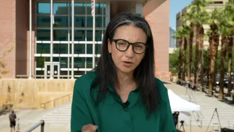 A woman in glasses and a green shirt stands in front of a court house in Las Vegas.