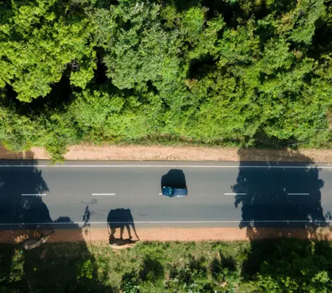 Supun Dilshan A drone image of elephants walking along a road as a car passes by