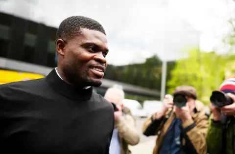 A man in black top is surrounded by photographers. 