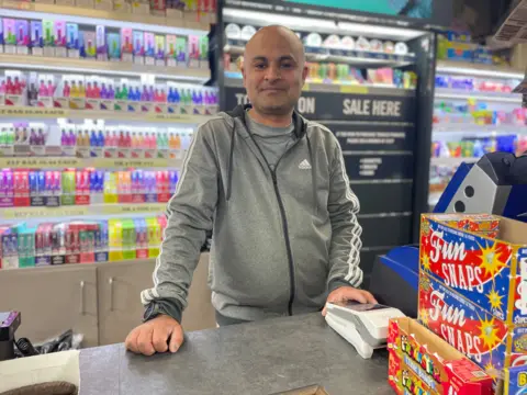 Shopkeeper Urfan Hussain at the till in his local grocery shop