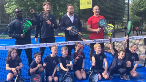 A group of children on a tennis court, with comedian Jason Manford