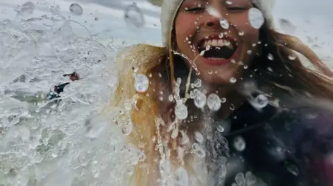 Linda Todd Young woman splashing in sea water, with a wide smile.