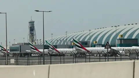 Three Emirates planes lined up at Dubai International Airport, a control tower stands in the background.