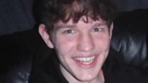 Police Scotland Alexander is smiling at the camera. He has short brown hair and is wearing a black top.