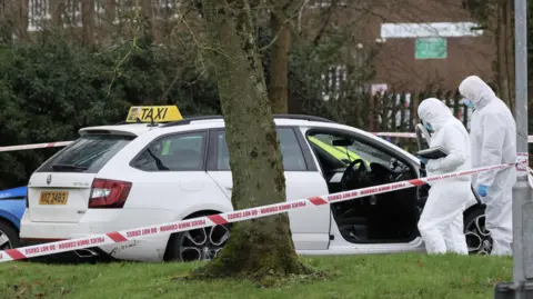 Pacemaker Two men in hazmat suits peer into a white taxi. There is a police cordon saying, 'do not cross' on it