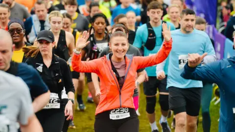 Kettering Town Council A woman in an orange raises her arms as she runs in a field.