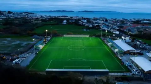 Handout A football pitch from above on an evening with buildings surrounding it and the sea visible in the distance.