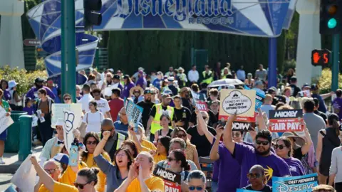 Getty Images Hundreds of Disneyland workers are seen with signs protesting outside the park's gates 