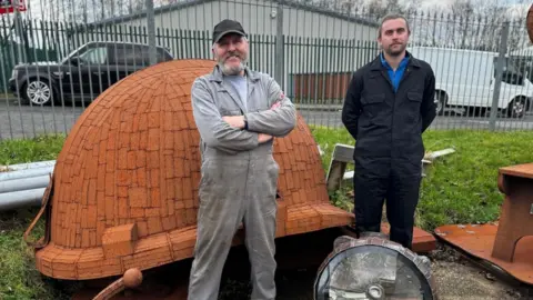 BBC Ray and Sam Lonsdale standing in front of a mining helmet sculpture almost as tall as they are