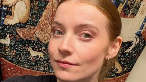 Dr Daisy Dixon Close up photo of Dr Daisy Dixon. Her light brown hair is slicked back. She has a piercing underneath her lip, a septum piercing and an ear piercing. 