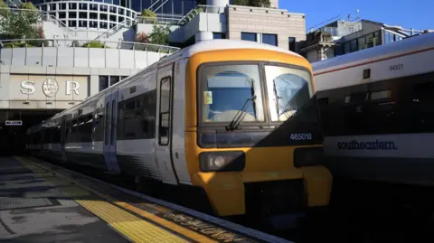 Two Southeastern trains stopped at platforms at Charing Cross station. The station building is in the background with the letters SR written on it