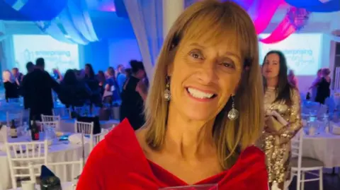 Think Pink Mary wearing a red dress and silver earrings smiling for the camera. She appears to be at an awards evening.