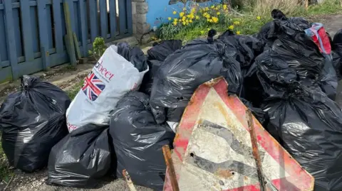 Weymouth & Portland Marine Litter Project Rusty road sign propped against black bags of rubbish piled up.