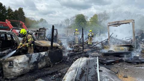 Firefighters spray water over a fire-damaged scrap yard