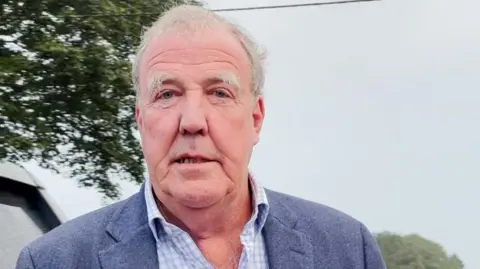 PA Jeremy Clarkson looking at the camera and wearing a blue and white check shirt with a blue blazer