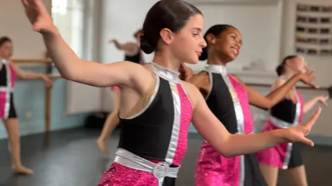 A group of girls dancing in black, pink and silver dresses in a dance studio