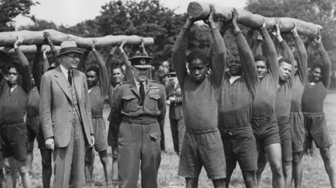 A group of RAF recruits from the Caribbean undertaking physical exercises in front of a number of military officials