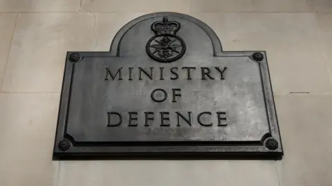 Ministry of Defence written on a dark plaque attached to a wall. 