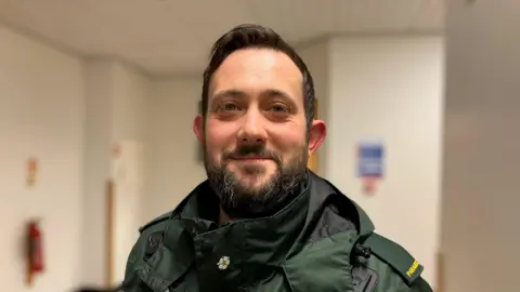Paramedic Shane Guinan stands in a hospital corridor wearing his uniform.