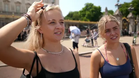 Two women with blonde hair interviewed in front of Buckingham Palace