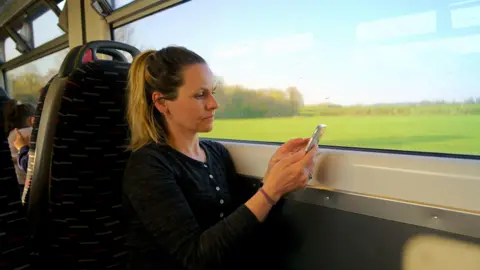 A woman sits alone on a speeding train reading from her mobile phone.