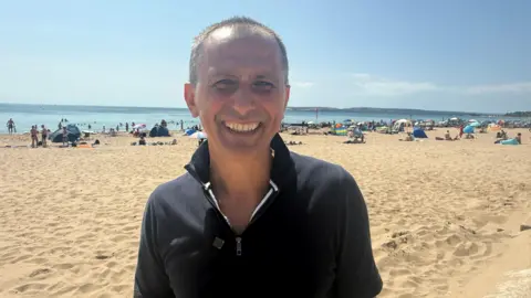 A man smiling stood on the beach.