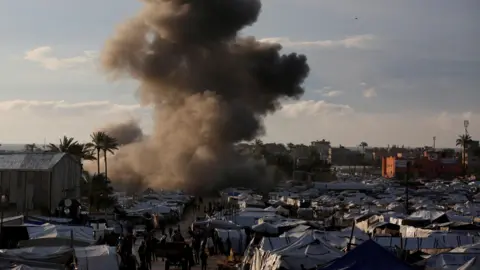 Reuters Smoke can be seen rising behind a tent camp following an Israeli strike in the central Gaza strip